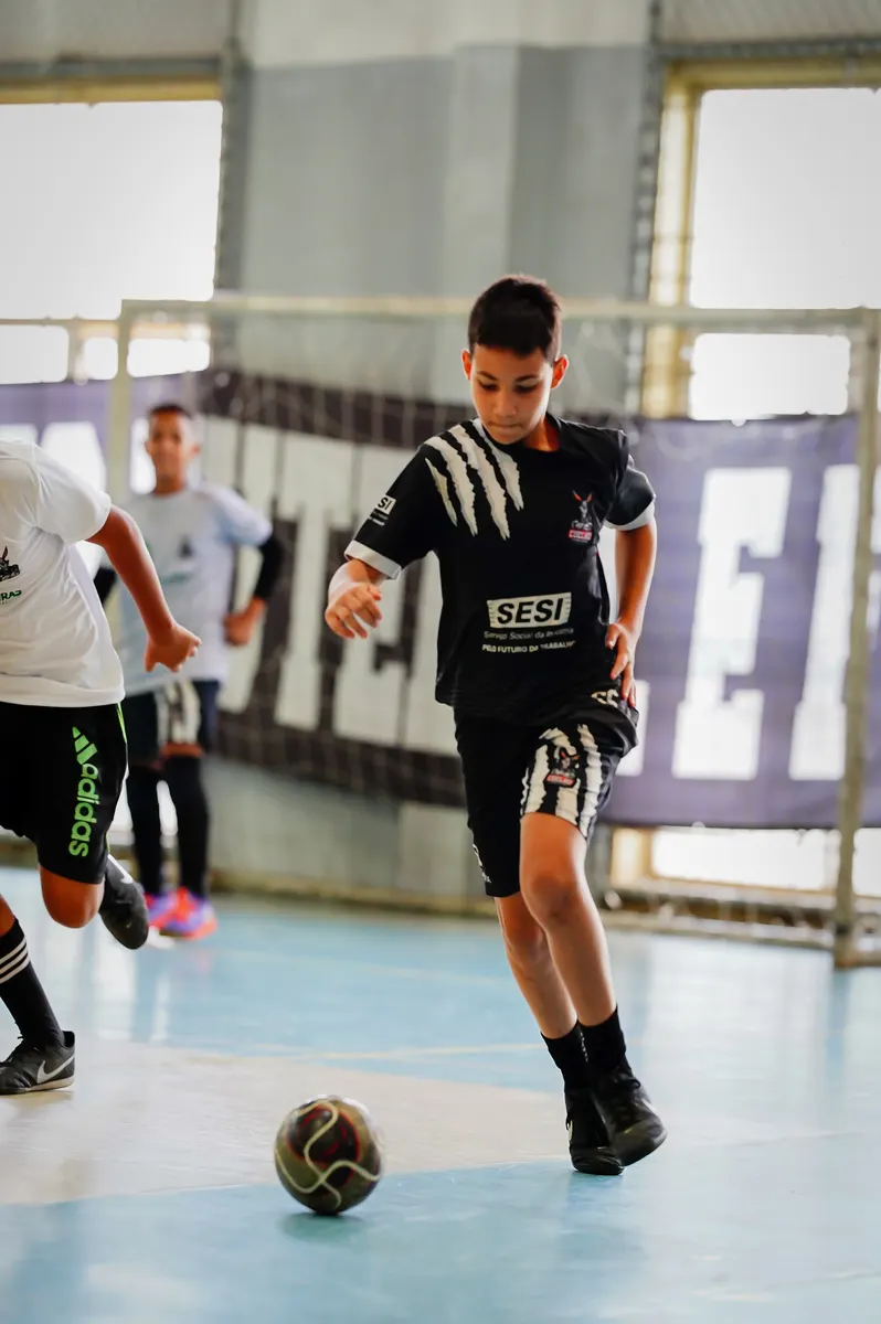 Aluno conduzindo a bola na quadra de futsal